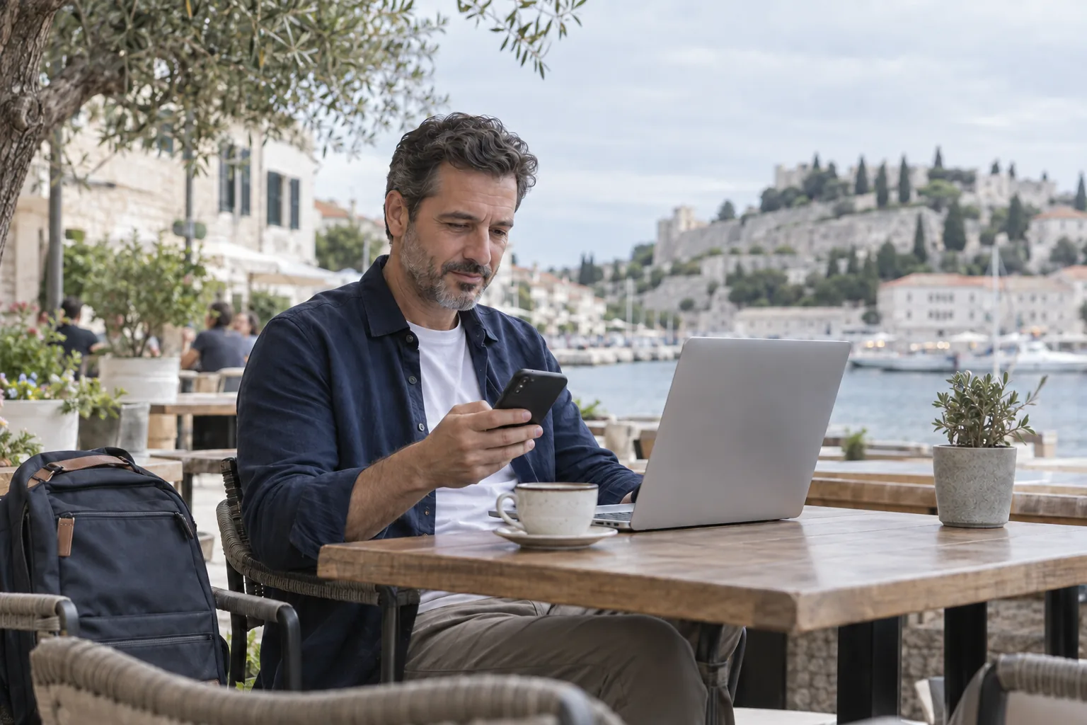 Kafe terasında dizüstü bilgisayarı ve telefonuyla çalışan bir kişi
